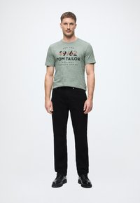 Πράσινο μαντζέντα μπλουζάκι με μαύρη εκτύπωση, συνδυασμένο με στενά μαύρα τζιν. Το σύνολο ολοκληρώνεται με μαύρες φλάντζες μποτες.