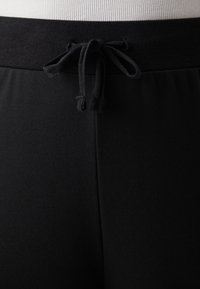 Czarne spodnie z elastycznym paskiem w talii i sznurkiem z przodu, o gładkiej fakturze i dopasowanym kroju.