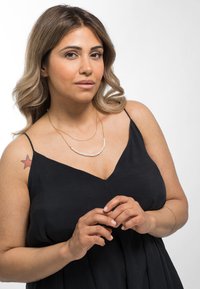 Collier en or superposé avec des perles blanches, port�é sur une robe noire sans manches. Texture lisse et design simple avec un décolleté en V.