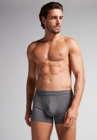 Graue Boxershorts aus Baumwolle mit konturiertem Beutel, elastischem Bund und glatter Textur, getragen von einem Modell mit muskulösem Körperbau.