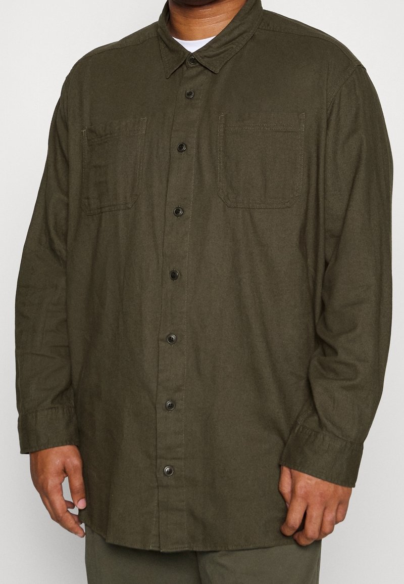Camicia verde con bottoni realizzata in tessuto testurizzato, con colletto, due tasche sul petto e bottoni neri.