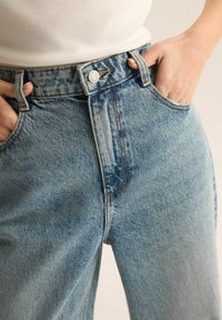 Jasnoniebieskie dżinsy z wysokim stanem, z przednimi kieszeniami, zapięciem na guzik oraz widocznym szwem wzdłuż szwów.