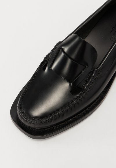 Mocassins en cuir noir avec un bout sculpté, des coutures décoratives et une semelle plate. Présentent un accent surélevé à l'avant pour un détail supplémentaire.
