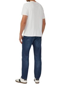 Biała koszulka z krótkim rękawem i okrągłym dekoltem, zestawiona z ciemnoniebieskimi dżinsami z kieszeniami i prostą nogawką, uzupełniona białymi trampkami.