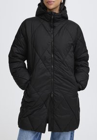Veste en duvet noire matelassée avec une capuche, dotée d'une fermeture éclair à l'avant, de poches latérales et d'un motif en losanges sur le tissu.