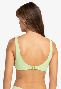 Lys grønn ribbet bikini-top med brede stropper og baklås. Glatt tekstur med rund form og ingen ekstra mønstre eller detaljer.