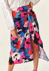 Falda con estampado floral que presenta colores vibrantes como rosa, azul y negro. La tela parece ligera, con una abertura lateral y un detalle de nudo en la cintura.