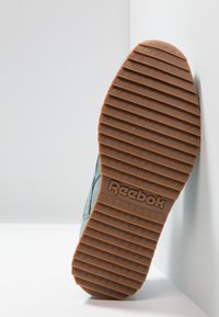 Reeboksneakersula i brun gummi med vertikala spår, delvis synlig ljusblå mocka övre, lutad mot en vit bakgrund.