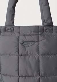 Borsa tote grigia trapuntata con manici imbottiti e un piccolo logo impresso centrato sul pannello frontale.