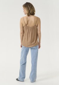 Haut sans manches marron avec un détail froncé au dos, associé à un jean évasé bleu clair. La tenue présente un design minimaliste et un tissu doux.