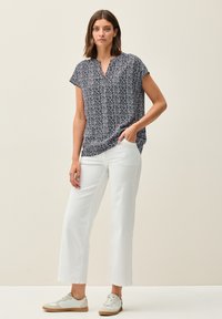 Marineblå mønstrede bluse med korte ærmer og V-hals, parret med hvide vide bukser og lyse sneakers. Glat stof med geometrisk design.