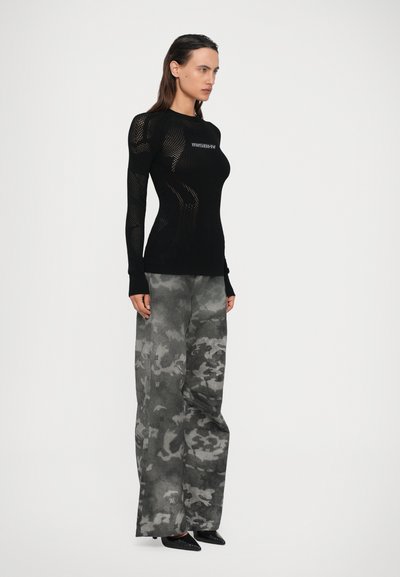 Haut à manches longues en mesh noir avec logo, associé à un pantalon ample gris avec motif camouflage. Porté avec des chaussures noires à bout pointu.