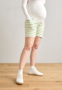 Mammabukser i lett stoff med grønne og hvite horisontale striper, med sidelommer og et tettsittende midjebånd, kombinert med hvite sneakers.