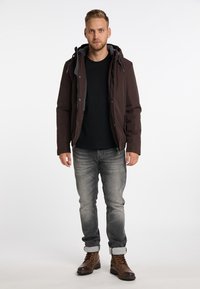 Brun zip-up hættetrøje med grå foer, sort skjorte, grå jeans med opkrøllede bukseben og brune snørebåndsstøvler. Ensfarvet baggrund.