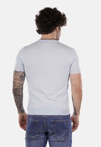 Maglione a maniche corte di colore azzurro chiaro realizzato in maglia, con colletto e orlo a costine. Texture liscia con un design aderente, indossato con jeans in denim scuri.