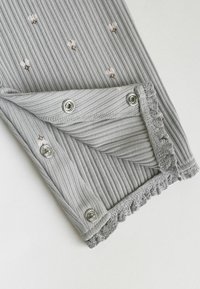 Tissu gris côtelé avec petits motifs floraux, avec boutons-pression métalliques et bordure en dentelle pour la fixation.