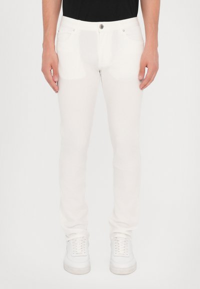 Białe, slim-fit jeans o gładkiej fakturze, pięć kieszeni, metalowe zapięcie na guzik oraz detale ściegów, w połączeniu z białymi sneakersami.