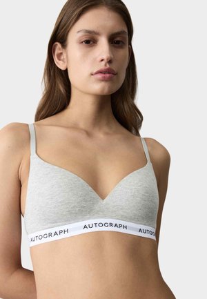 Kvinde iført en grå soft-cup bh med tynde justerbare stropper og en hvid elastik med mærket "AUTOGRAPH" mod en ensfarvet baggrund.