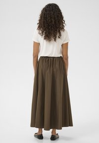 Gonna marrone a lunghezza piena realizzata in tessuto leggero con vita elastica, abbinata a una semplice t-shirt bianca e scarpe flat nere.