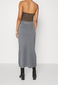 Grå ribbad stickad kjol, ankellång, med en åtsittande midja. Stylad med en mörkbrun axelbandslös topp och svarta ankelskor.