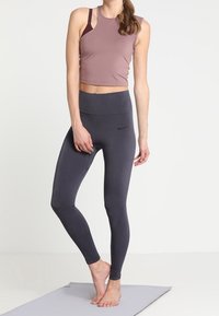 Helles mauve-farbenes, kurzes Tanktop kombiniert mit hochgeschnittenen, dunkelgrauen Leggings. Die Leggings haben eine dezente Textur und ein kleines Logo an der Seite.