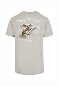 Helles graues Baumwoll-T-Shirt mit einem Rückendruck eines weißen Vogels im Flug und dem Text "Glaube über Angst" in geschwungener Schrift darüber.
