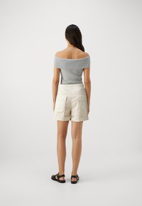 Svetlošedý off-shoulder rebrovaný top s bielymi cargo šortkami s bočnými vreckami a skrátenými okrajmi, skombinované s čiernymi sandálmi.