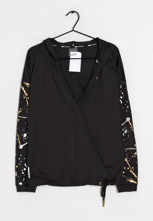 Chaqueta negra con capucha y cremallera frontal, diseño de pintura salpicada en las mangas, colgada en una percha negra sobre fondo blanco.