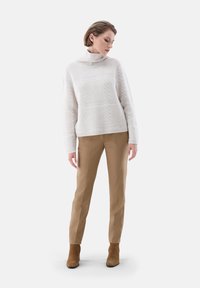 Weißer Strickpullover mit hohem Kragen und strukturiertem Muster, kombiniert mit beigen maßgeschneiderten Hosen und braunen Stiefeletten.