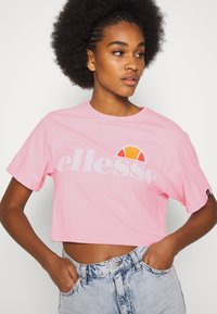 Pink cropped t-shirt with rolled sleeves featuring the brand name "ellesse" and a multicolored logo. Soft cotton material, casual fit.