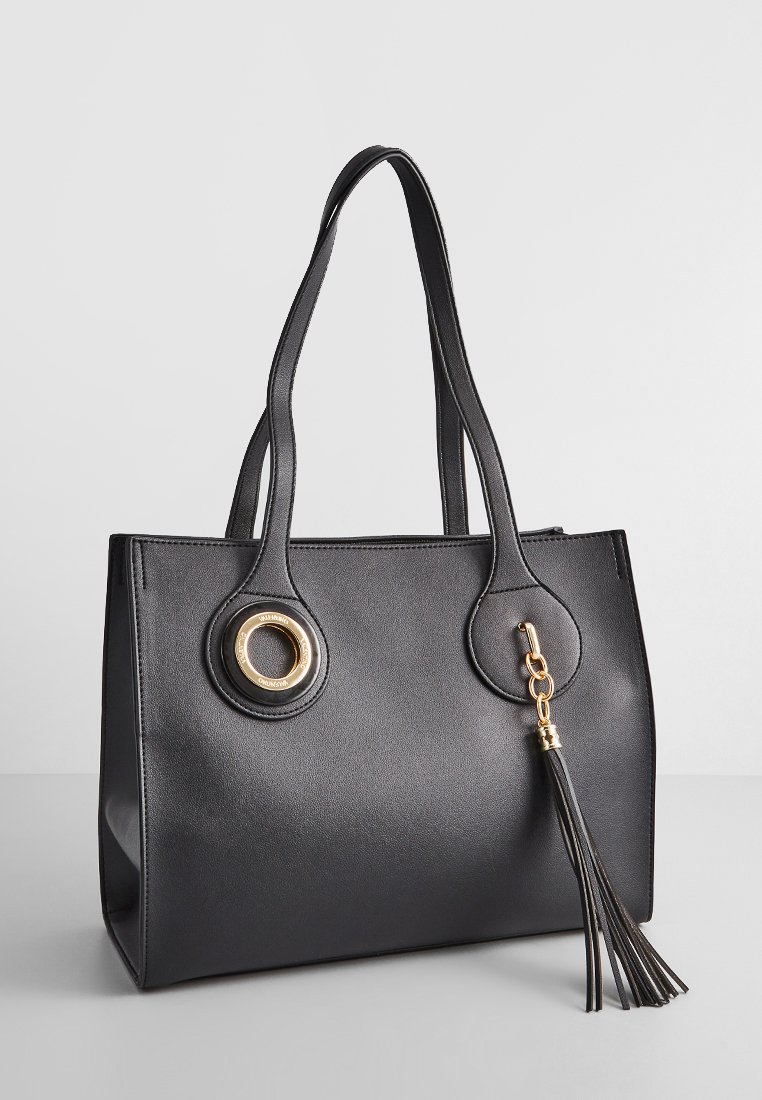 Sac fourre-tout synthétique noir avec deux poignées, accents en métal doré, un détail en oeillet rond et une frange décorative sur le côté. Forme rectangulaire.