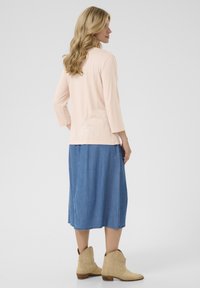 Helles rosa Oberteil mit drei Viertelärmeln, kombiniert mit einem Jeans-Midi-Rock und beigen Stiefeletten, mit einem lässigen Schnitt und weichen Materialien.