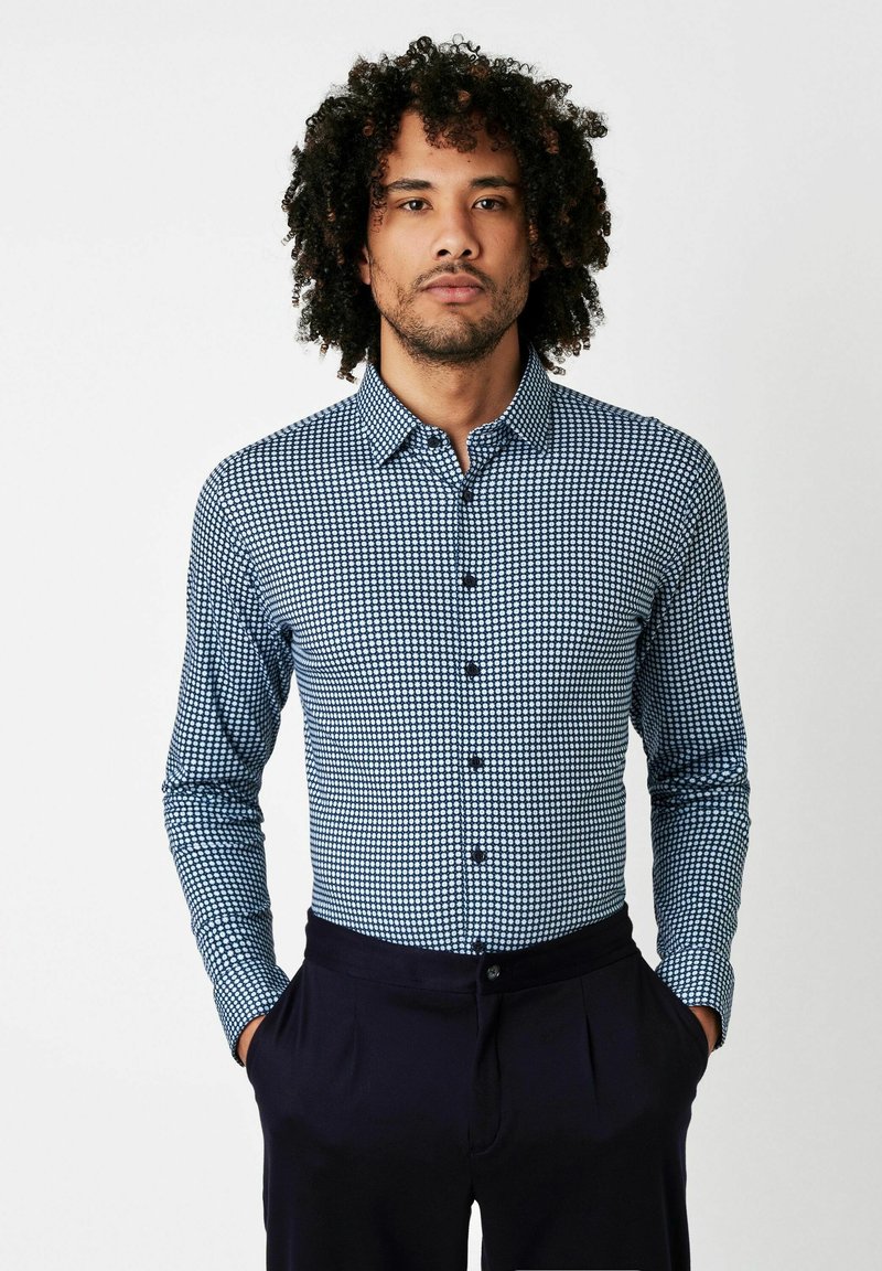 Blau-weiße kariertes Button-Up-Hemd mit langen Ärmeln und erstem Kragen, kombiniert mit dunklen Hosen. Hat ein tailliertes Design und einen abgerundeten Saum.