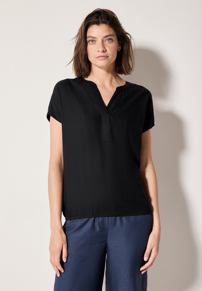Haut noir à manches courtes avec un décolleté en V et des coutures subtiles. Tissu léger et doux. Associé à un pantalon bleu marine ample.