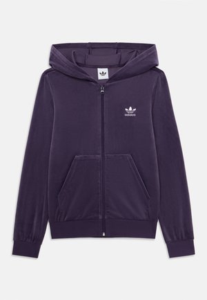 Felpa con zip di colore viola realizzata in tessuto morbido, dotata di tasca a marsupio, polsini a costine e logo Adidas ricamato in bianco sul petto.