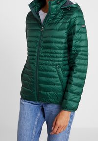 Grøn quiltet dunjakke med lynlås foran, høj krave og justerbar hætte. Designet med sidelommer og en figursyet silhuet.