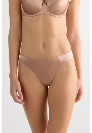 Kvinde iført nude-farvet bh og matchende højtaljede bikiniunderbukser, stående mod en ensartet lys baggrund.