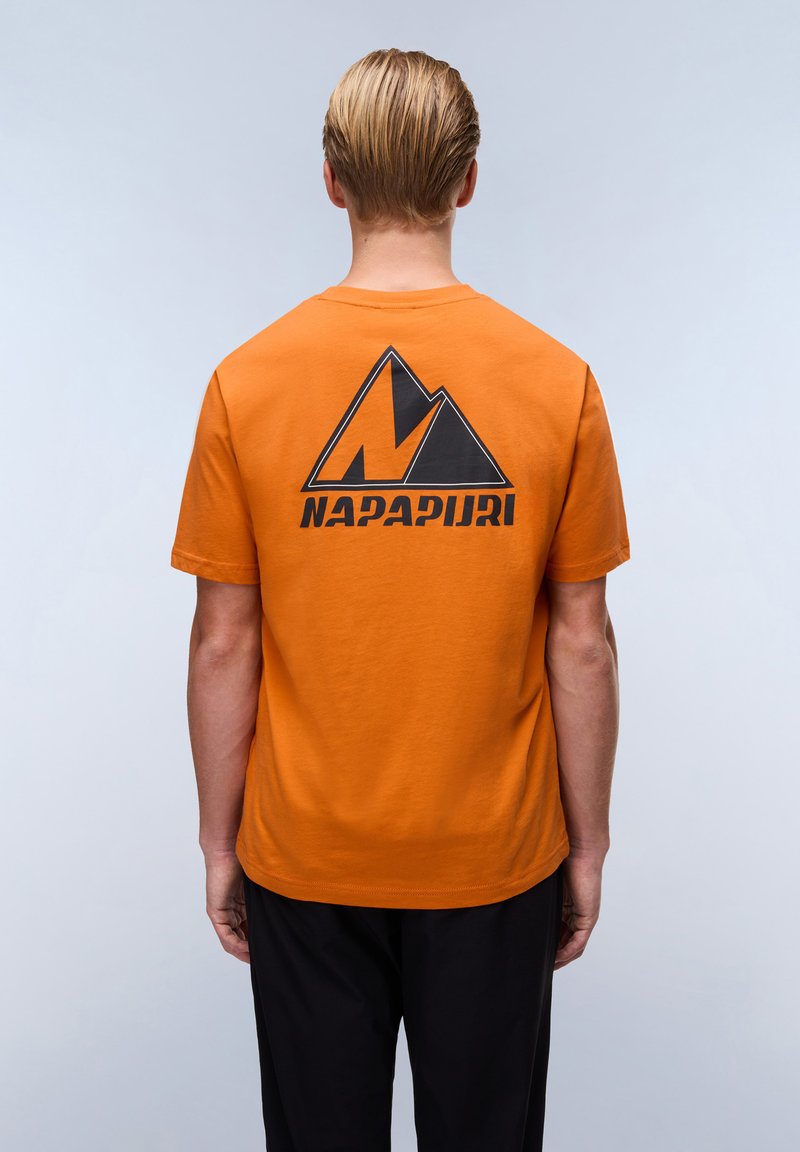 Orange bomulds t-shirt med et stort sort bjerg logo og "NAPAPIURI" tekst på ryggen. Korte ærmer, rund hals, afslappet pasform.