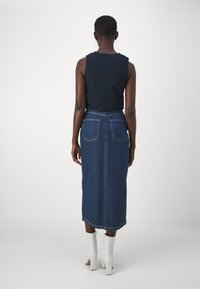 Pasagaliotas tamsiai mėlynas maikutė su ilgą tamsiai džinsinį sijoną, turinčių du užpakalinius kišenes ir baltus eina batus. Lygus tekstūra visame paviršiuje.