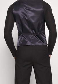 Elegante schwarze Satinweste mit tailliertem Schnitt, ausgestattet mit einer Rückenschnalle und seitlichen Einsätzen aus strukturiertem Stoff.