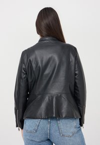 Giubbotto di pelle nera con orlo peplum, dotato di colletto a punta e polsini con zip, mostrato di spalle su uno sfondo chiaro.