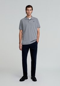 Grijze katoenen polo shirt met kraag, korte mouwen en een klein blauw logo. Gecombineerd met donkerblauwe broek en zwarte schoenen.