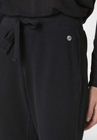 Schwarze Jogginghosen aus weichem Stoff, mit elastischem Bund und Kordelzug. Mit kleinem Logo auf der Vorderseite und Seitentaschen.