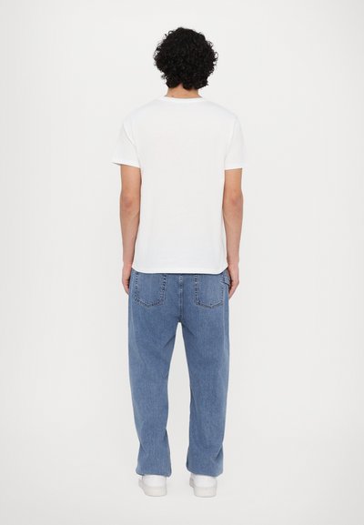 T-shirt en coton blanc avec un col rond, associée à un jean en denim bleu clair. Coupe ample avec deux poches arrière et design à jambes droites.