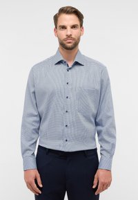 Camicia da uomo con bottoni in fantasia a scacchi, nei colori blu e bianco, maniche lunghe, una tasca e bottoni blu come dettaglio.