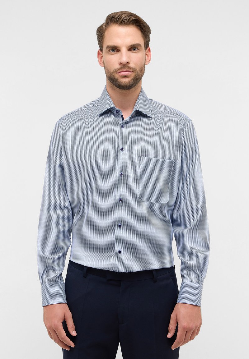 Camicia da uomo con bottoni in fantasia a scacchi, nei colori blu e bianco, maniche lunghe, una tasca e bottoni blu come dettaglio.