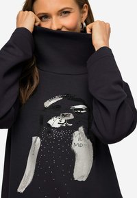 Felpa nera con colletto alto, caratterizzata da un design stampato di un volto di animale in argento e decorazioni in perline lungo il fondo.
