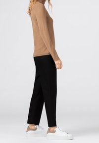 Tan rolák spárovaný s černými zúženými kalhotami a bílými teniskami s béžovými doplňky. Hladká pletená textura, přiléhavý střih.