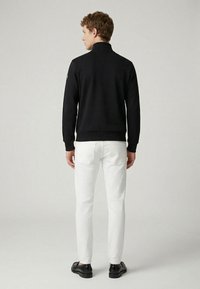 Black sweatshirt with a high collar, ribbed cuffs, and hem, paired with white slim-fit pants and black shoes. Simple design, no visible patterns.