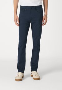 Pantalons en coton bleu marine avec une coupe slim, cinq poches et une fermeture à bouton. Accompagnés de baskets crème avec des semelles en gomme.